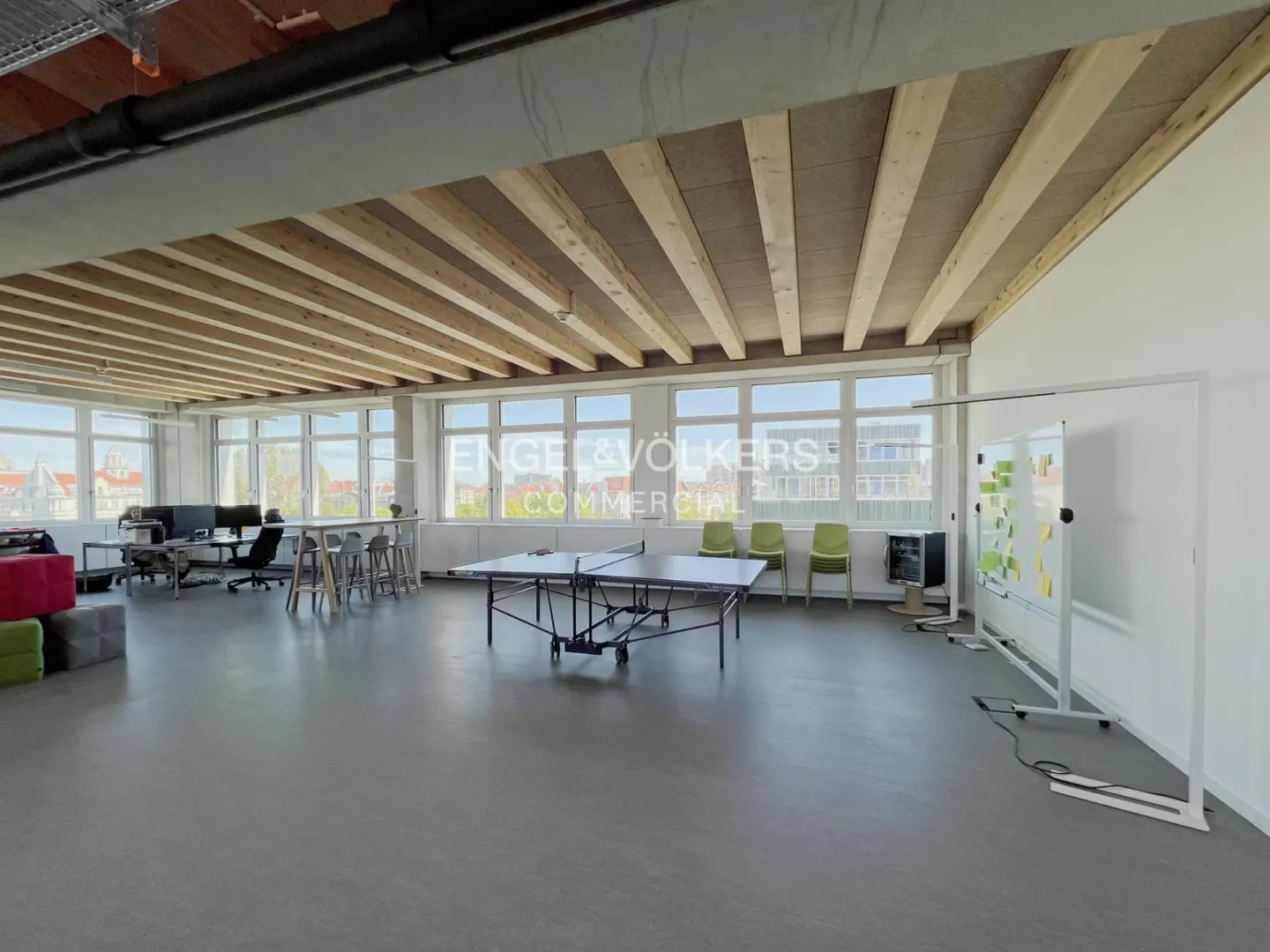 Bright, open office space with a ping pong table, desks, and a whiteboard. The ceiling has exposed wooden beams.