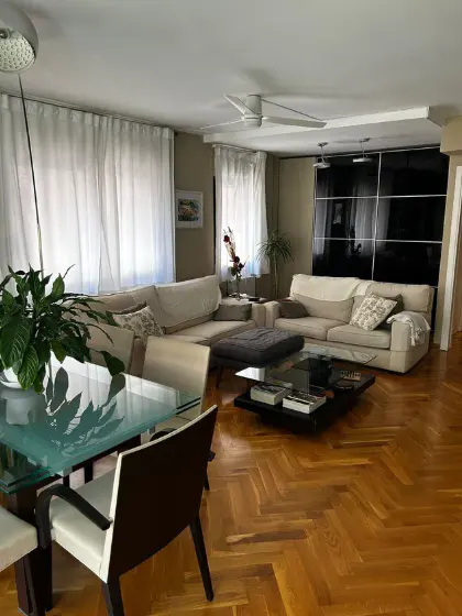 Living room with hardwood floors, beige sofas, a glass dining table, and large windows with white curtains.