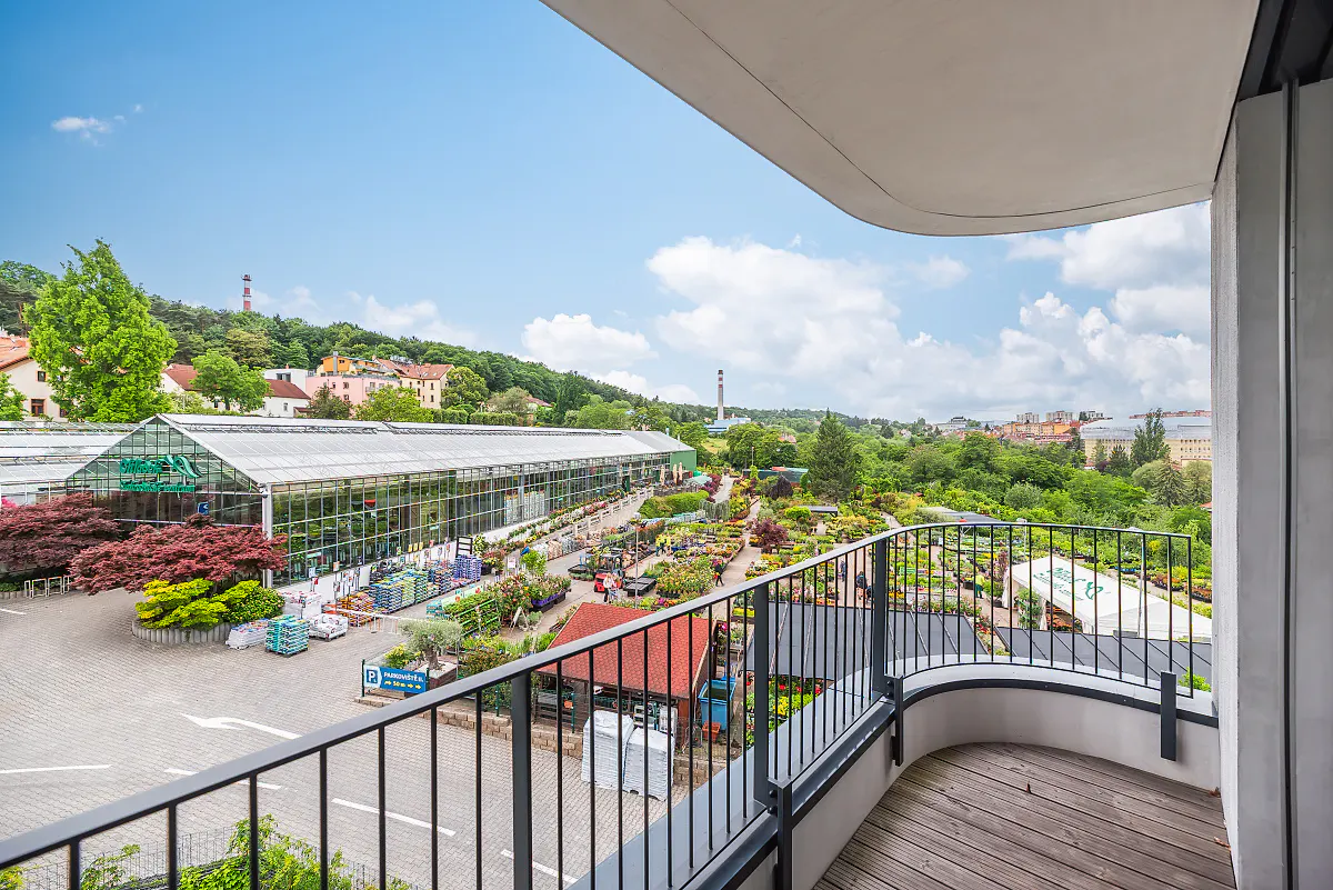 View from a balcony overlooking a large garden center with greenhouses, outdoor plant displays, and a paved parking area.