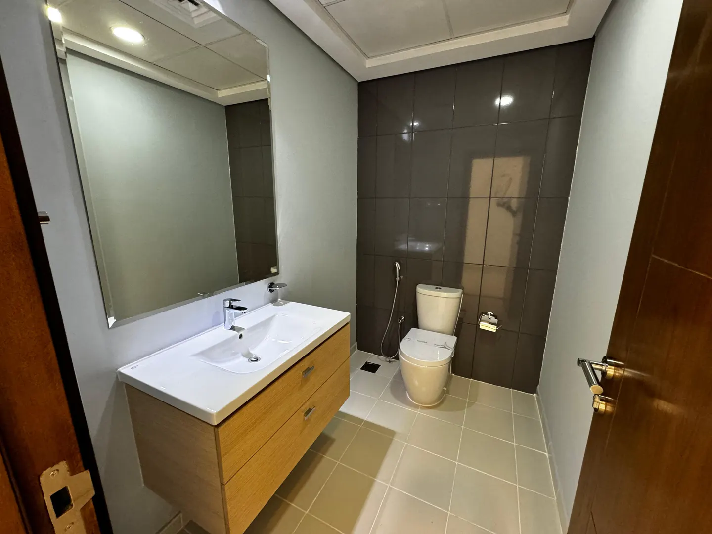 Bathroom with a white sink and wood cabinet, a toilet, and gray tile walls. A mirror hangs above the sink.