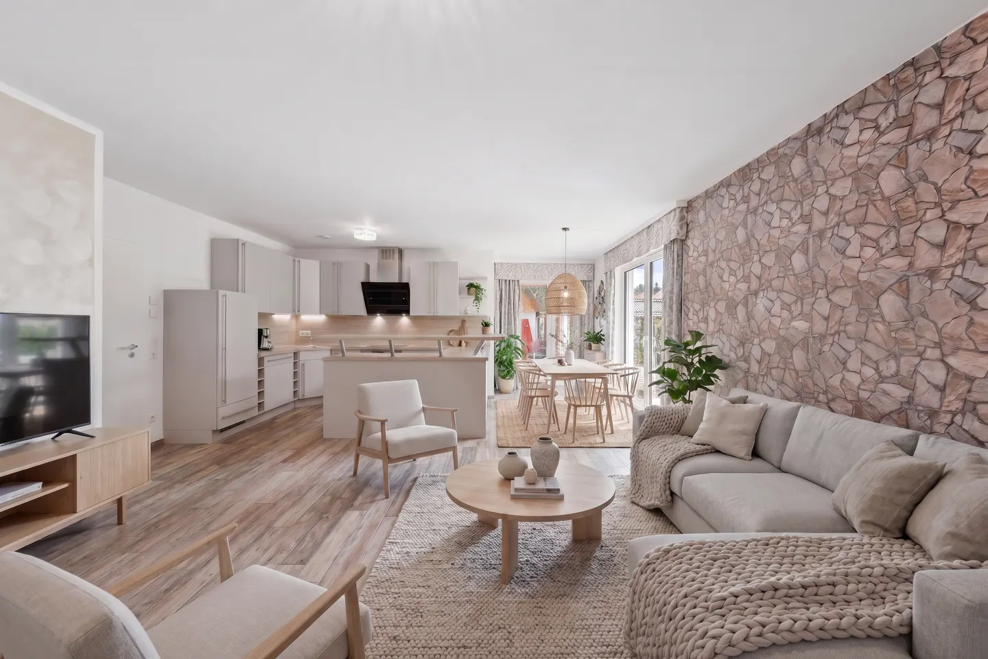 Open-concept living space with a stone accent wall, light gray sofa, wood floors, and a modern kitchen in the background.