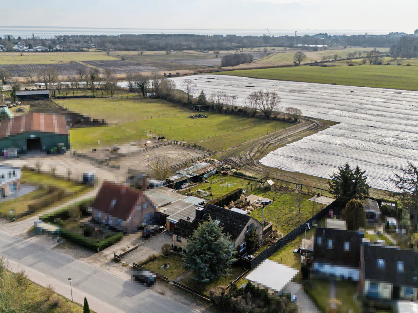 Aerial view of a rural property with houses, green fields, and a large white-covered field in the background.