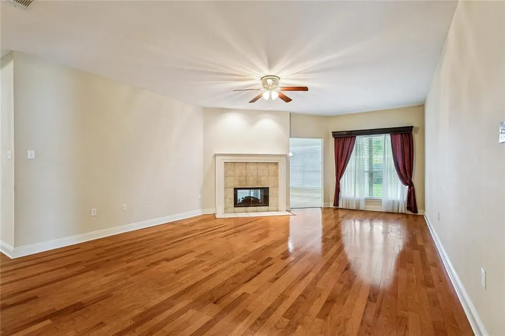 Bright living room with hardwood floors, a fireplace with tile surround, and a window with maroon curtains.