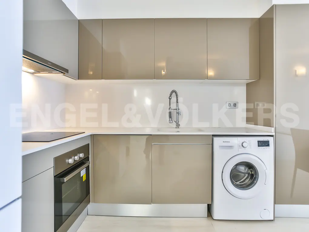Modern kitchen with beige cabinets, white countertops, stainless steel appliances, and a white washing machine.