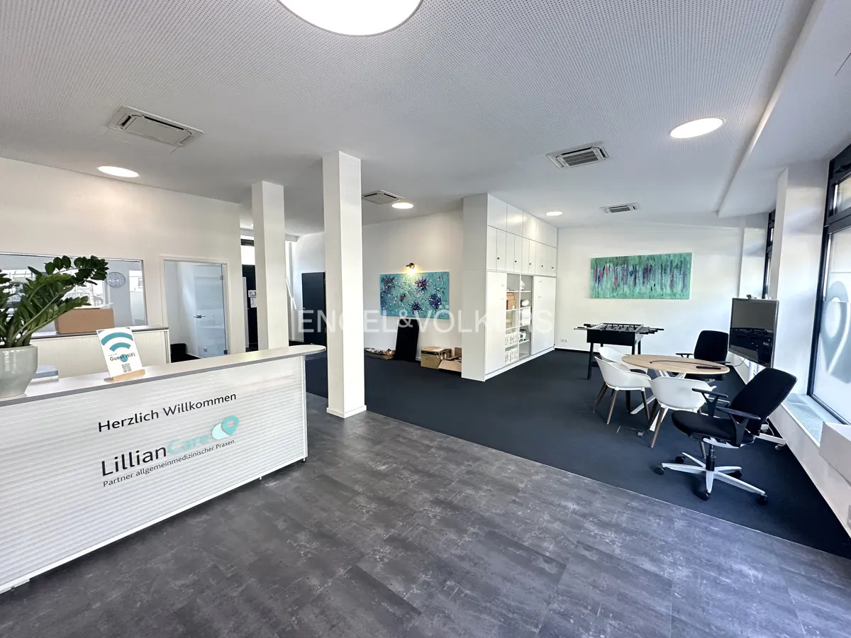 Bright office space with a reception desk, foosball table, and seating area. Gray floors and dark blue carpet. Artwork on the walls.
