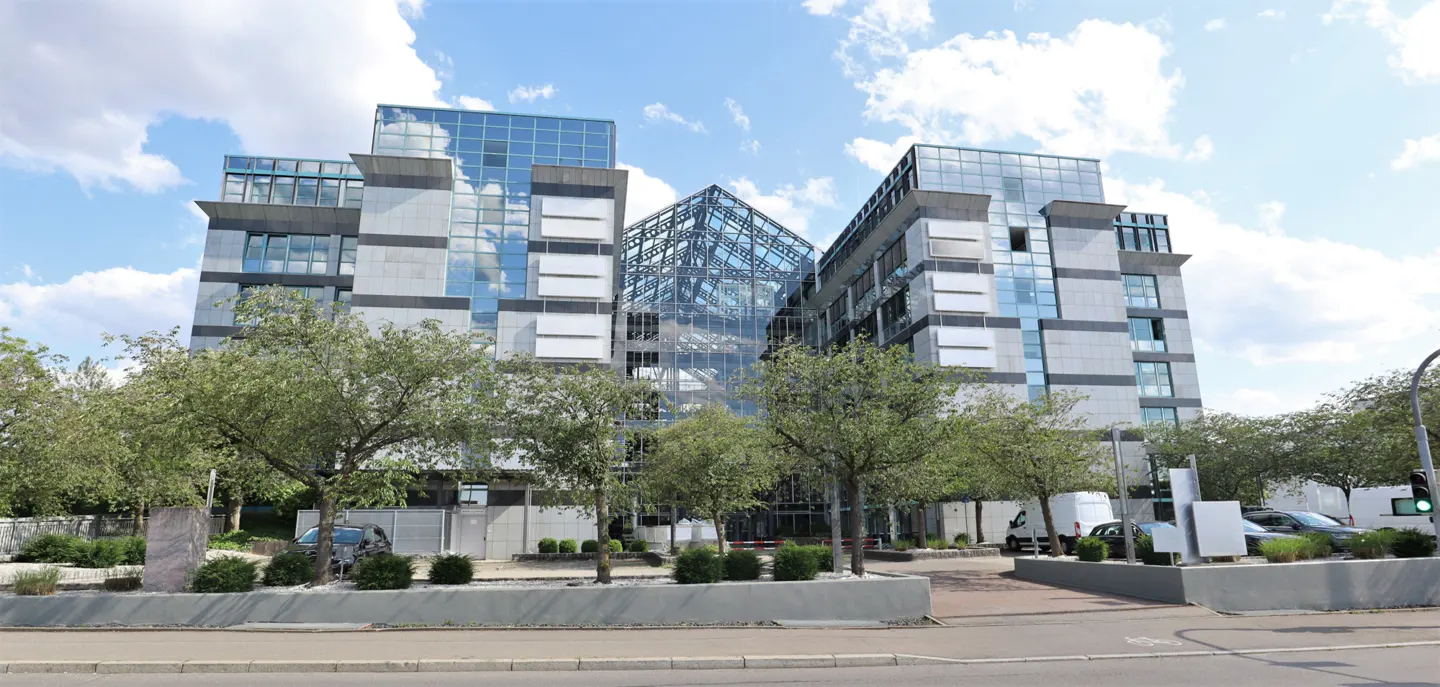Modern office building with glass and stone facade, trees in front, blue sky with clouds.
