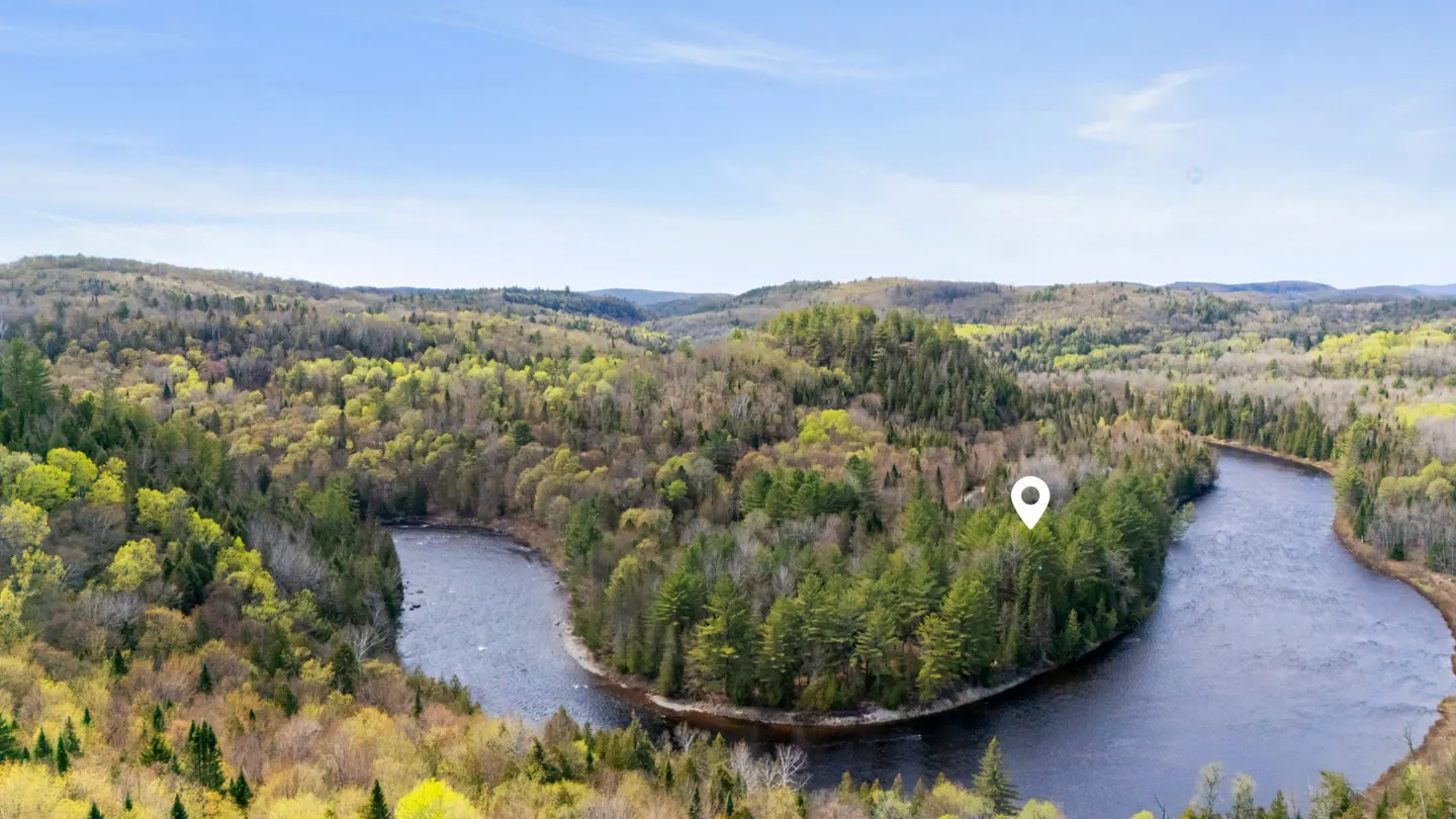 Aerial view of a winding river surrounded by green forest under a blue sky, with a location pin on the right side.