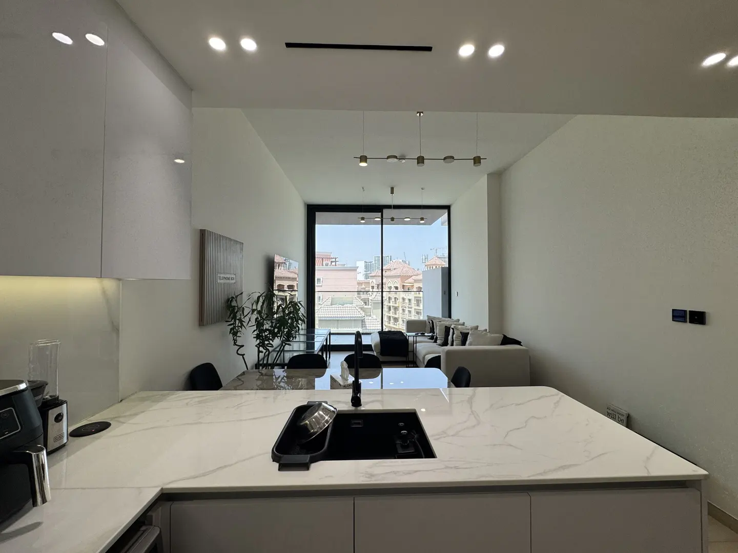 A modern apartment interior with a kitchen island, white cabinets, and a view of the city through a large window.