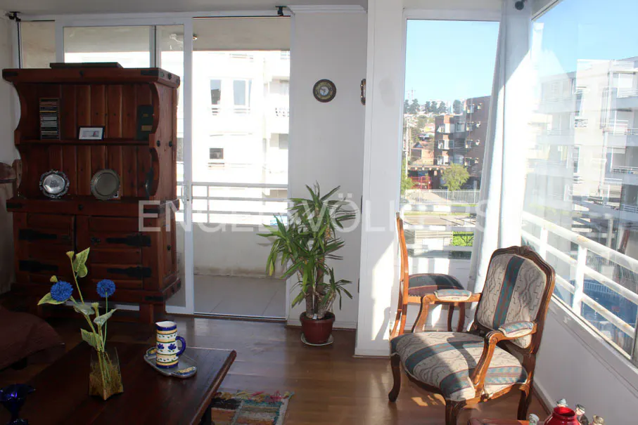 Living room with a wooden hutch, table with flowers, and chairs near a window with a city view.