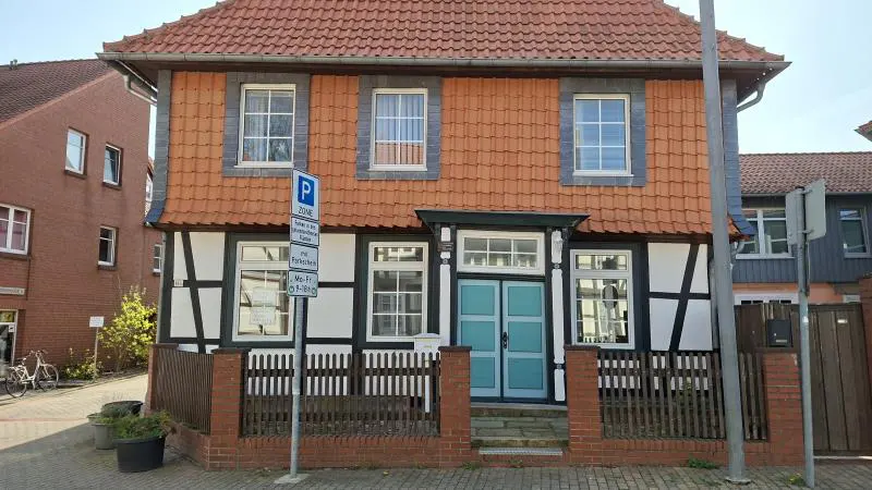Two-story half-timbered house with a red tile roof and a light blue door. A parking sign is in front of the house.
