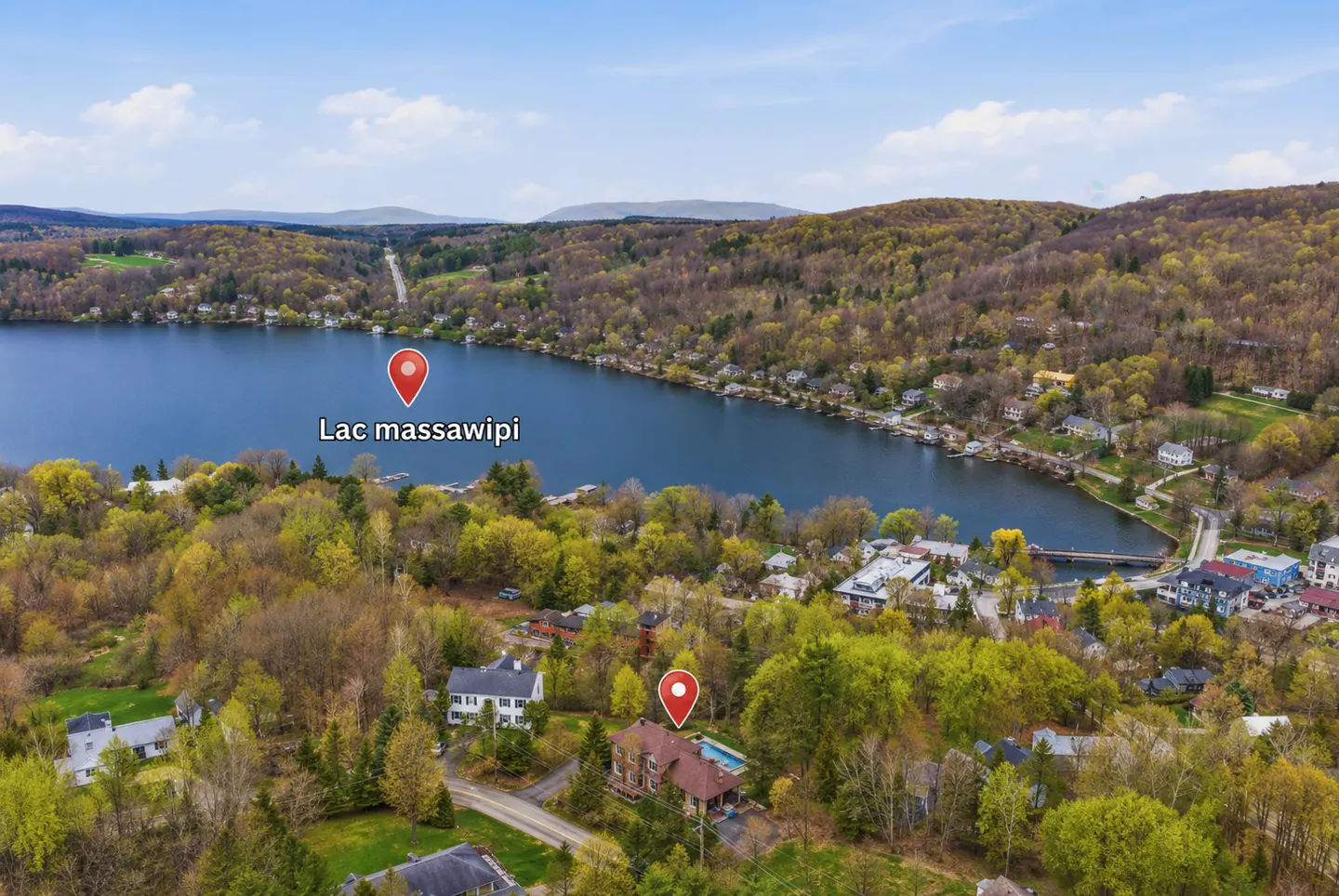 Aerial view of Lac Massawippi, Quebec, surrounded by green trees and houses. A red pin marks the lake's location.