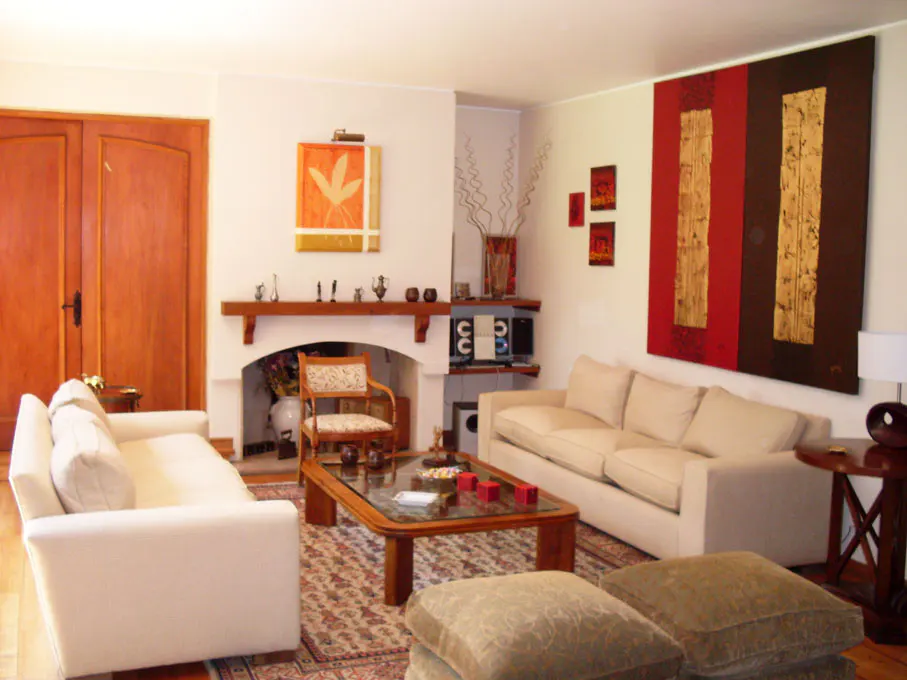 Living room with white sofas, a wooden coffee table, and a fireplace with decorative items. Artwork adorns the walls.