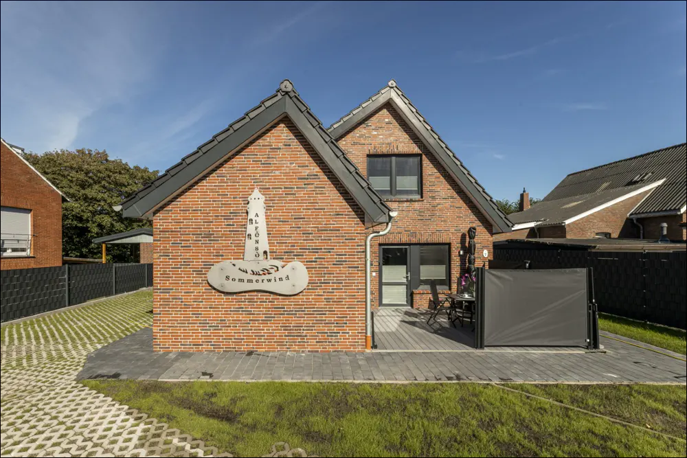 Exterior view of a brick house with a sign reading "Sommerwind" and a patio with furniture.