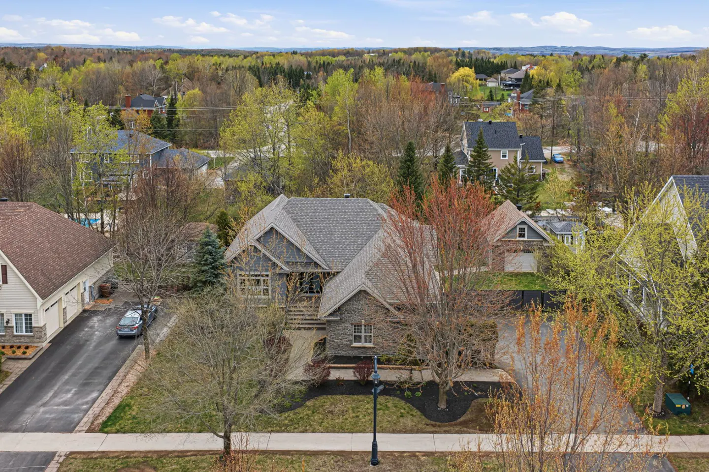 Aerial view of a gray stone house with a gray roof, surrounded by trees and other houses in a suburban neighborhood.