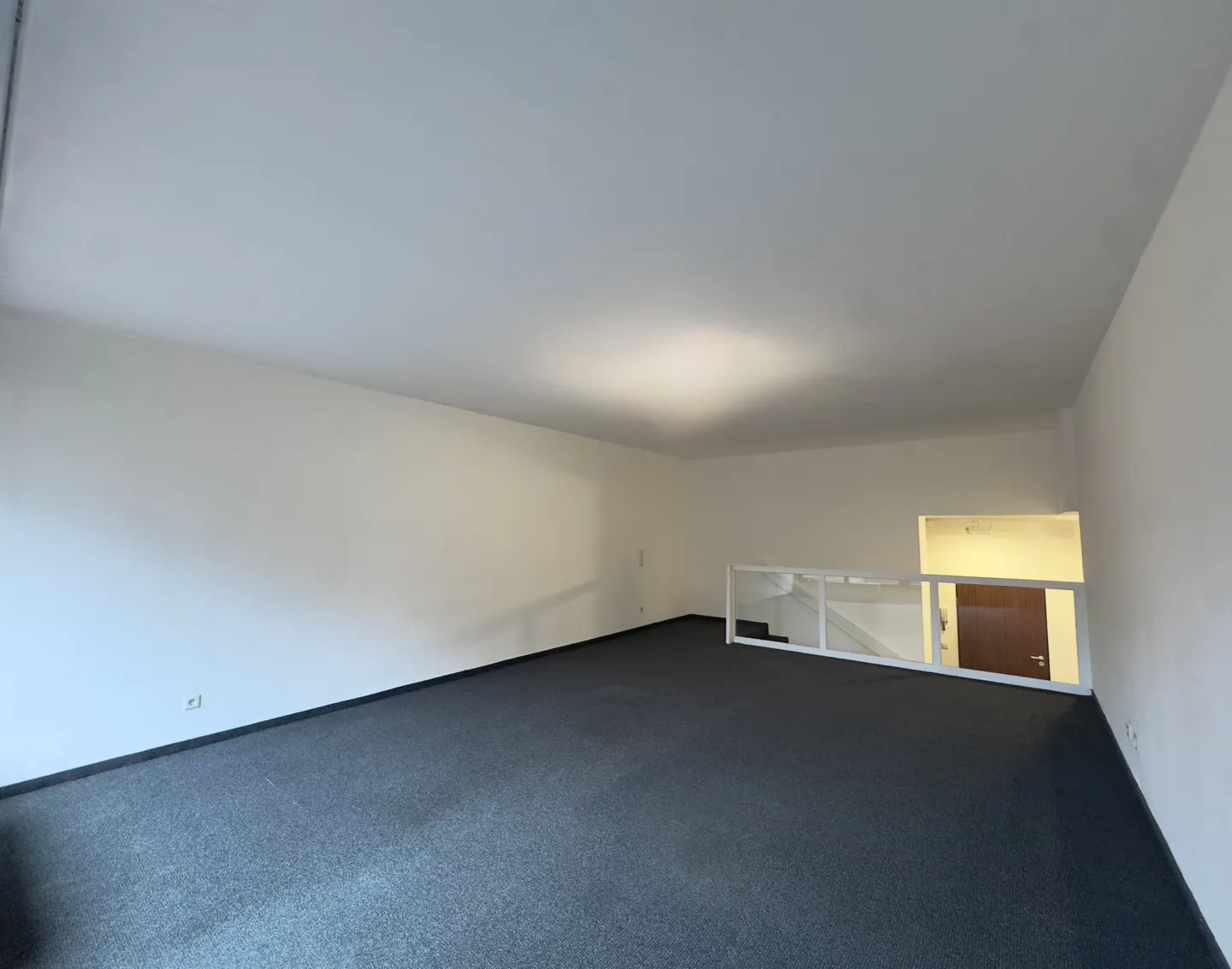 Empty room with white walls, gray carpet, and a white railing overlooking a door.