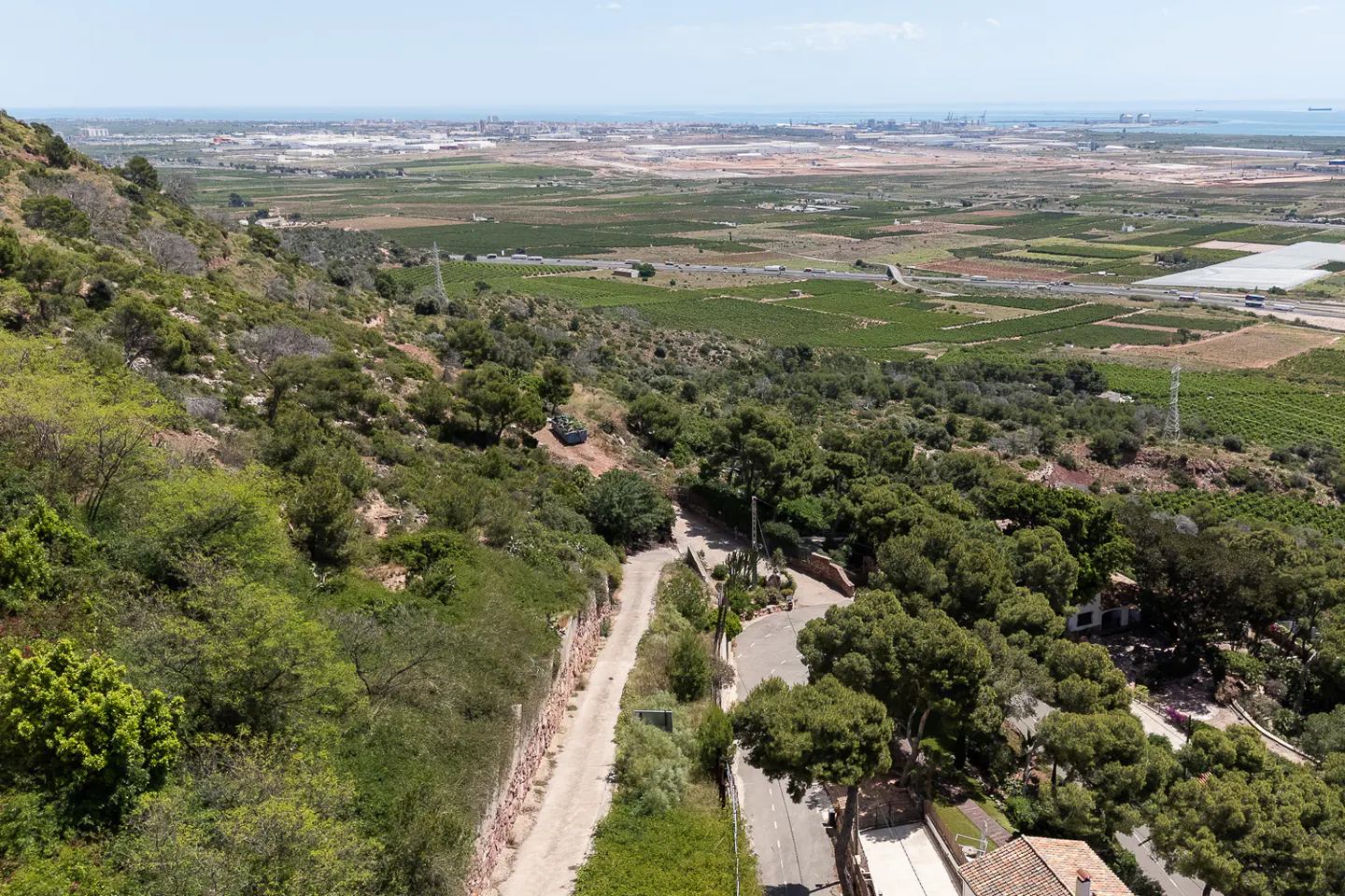 Scenic view from a green hillside overlooking a valley with fields, roads, and a distant cityscape by the sea.