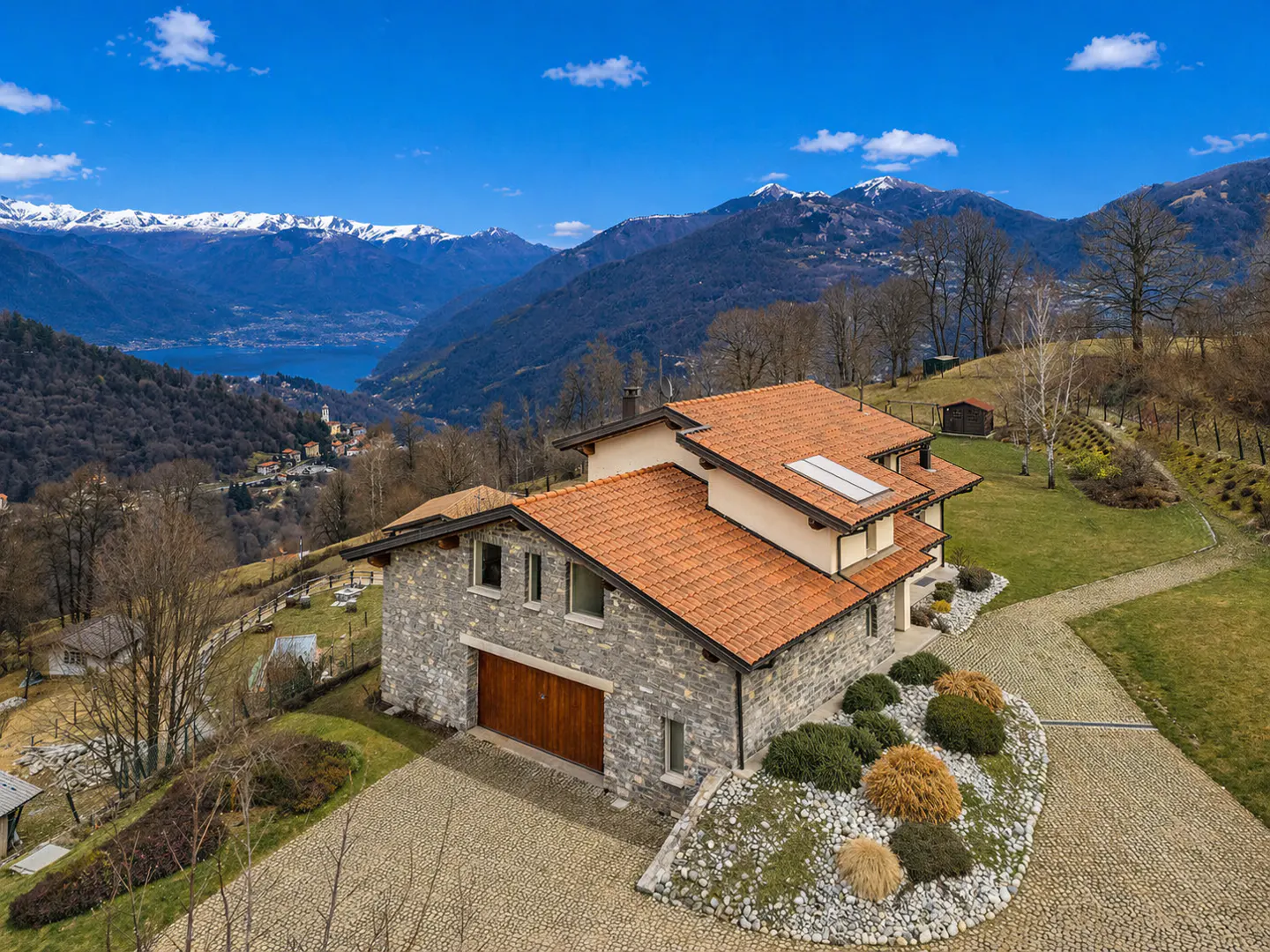 Stone house with a red tile roof, a wooden garage door, and a mountain view.