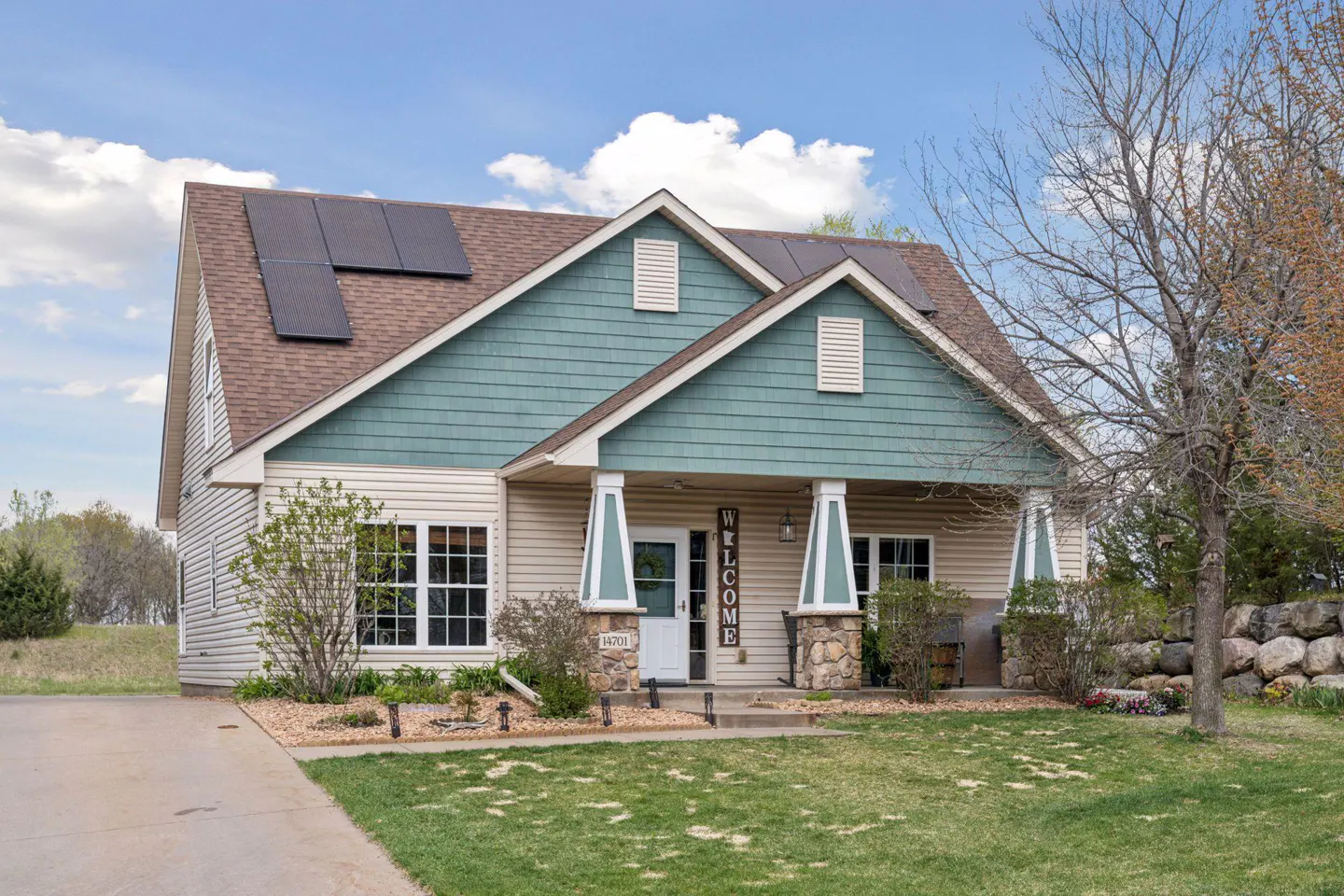 Beige two-story house with green trim, solar panels, and a "Welcome" sign on the porch.