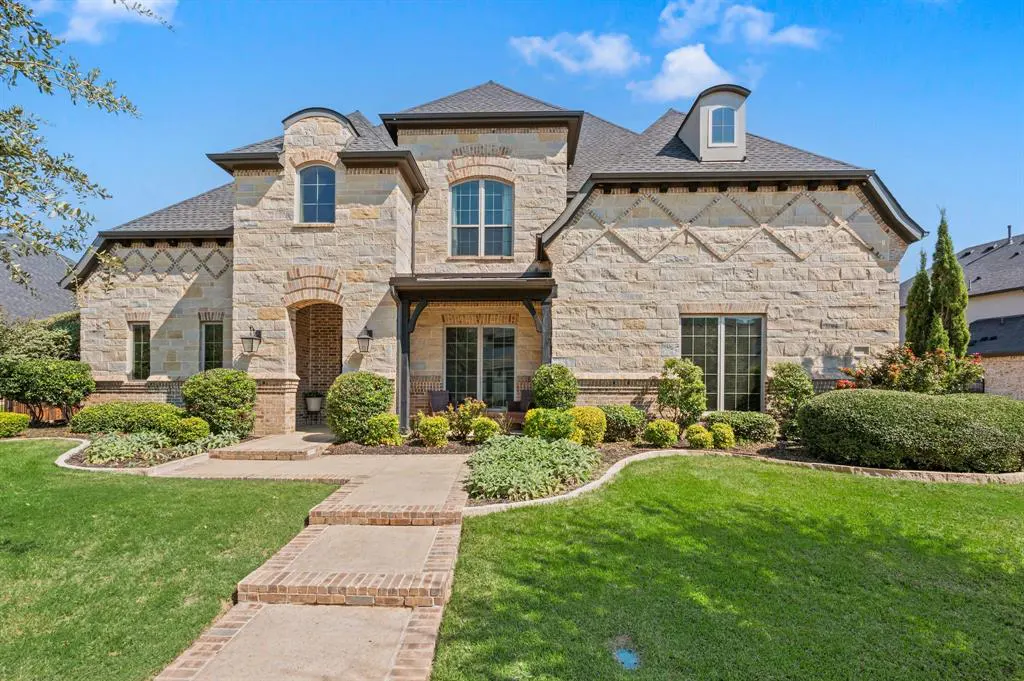 Two-story stone house with a gray roof, green lawn, and brick walkway under a blue sky.