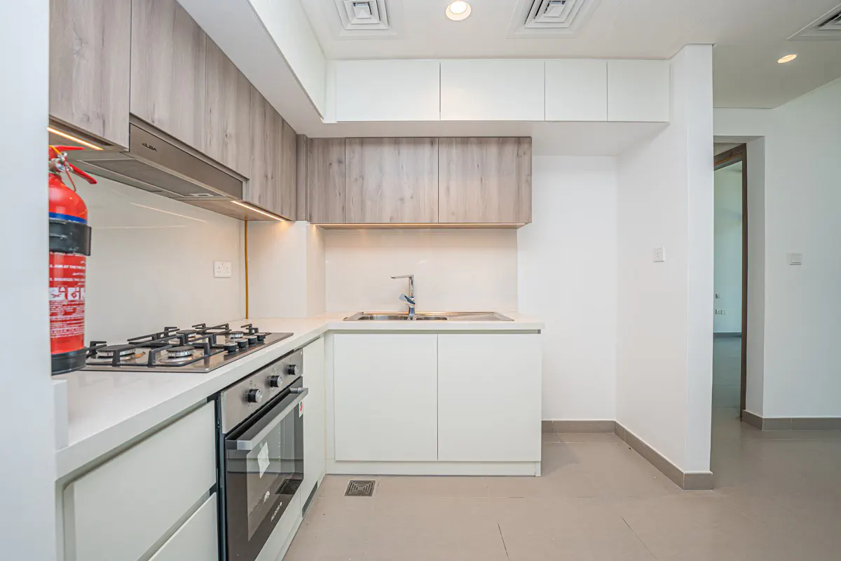 Modern kitchen with white cabinets, wood-tone upper cupboards, gas stove, oven, and a red fire extinguisher on the wall.