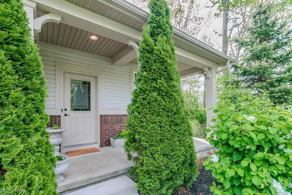 Front entrance of a house with a white door, brick accents, and green shrubs.