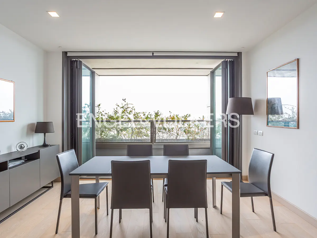 A modern dining room with a gray table, chairs, and a view of greenery through open glass doors.
