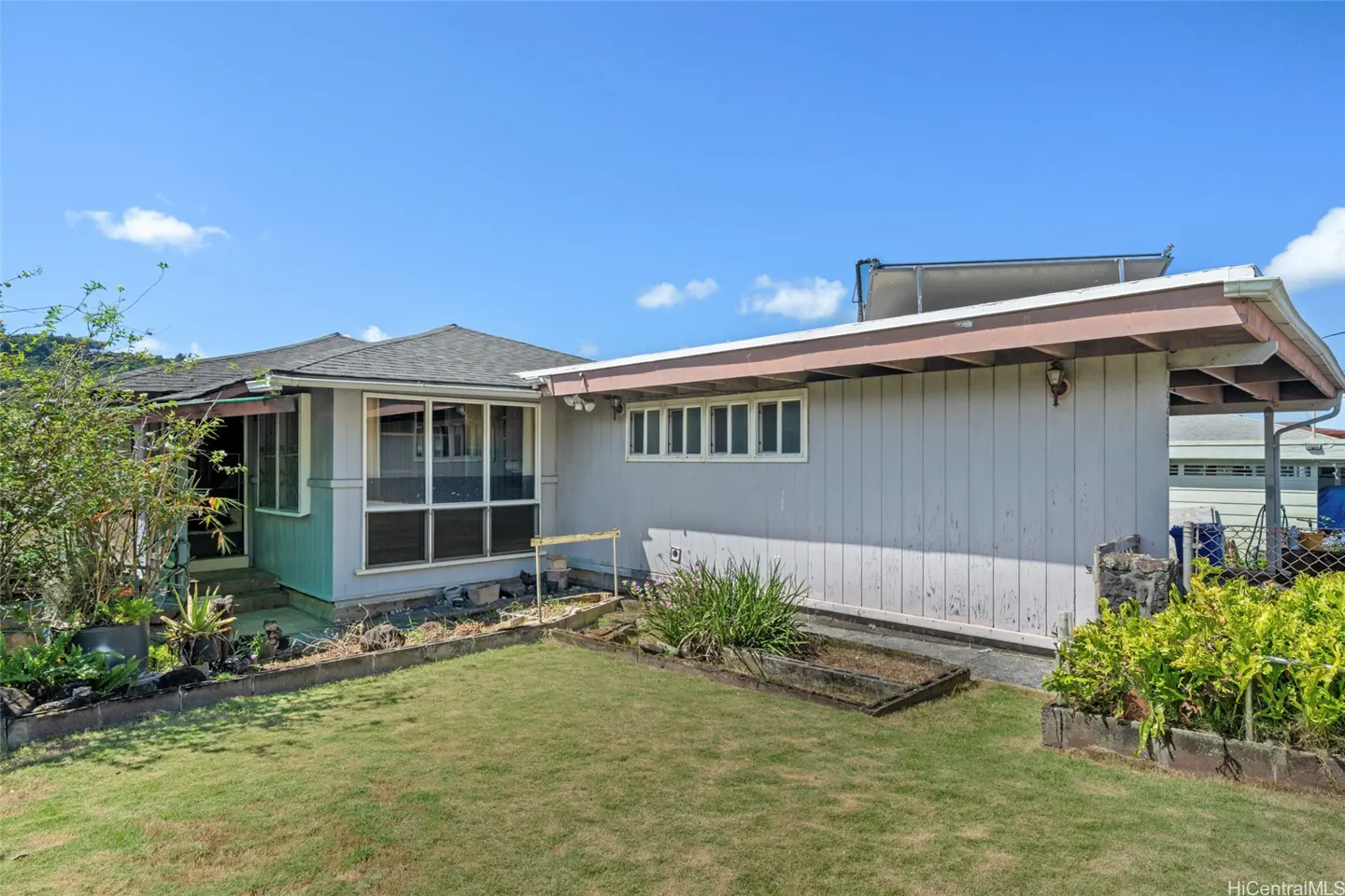 Backyard view of a single-story home with a gray exterior, green lawn, and blue sky. A screened-in porch is visible on the left.