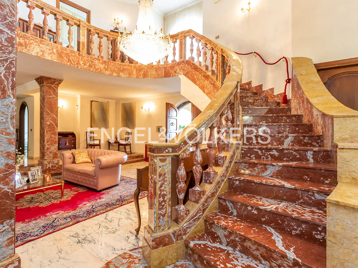 Interior view of a grand foyer with a marble staircase, crystal chandelier, and pink sofa.