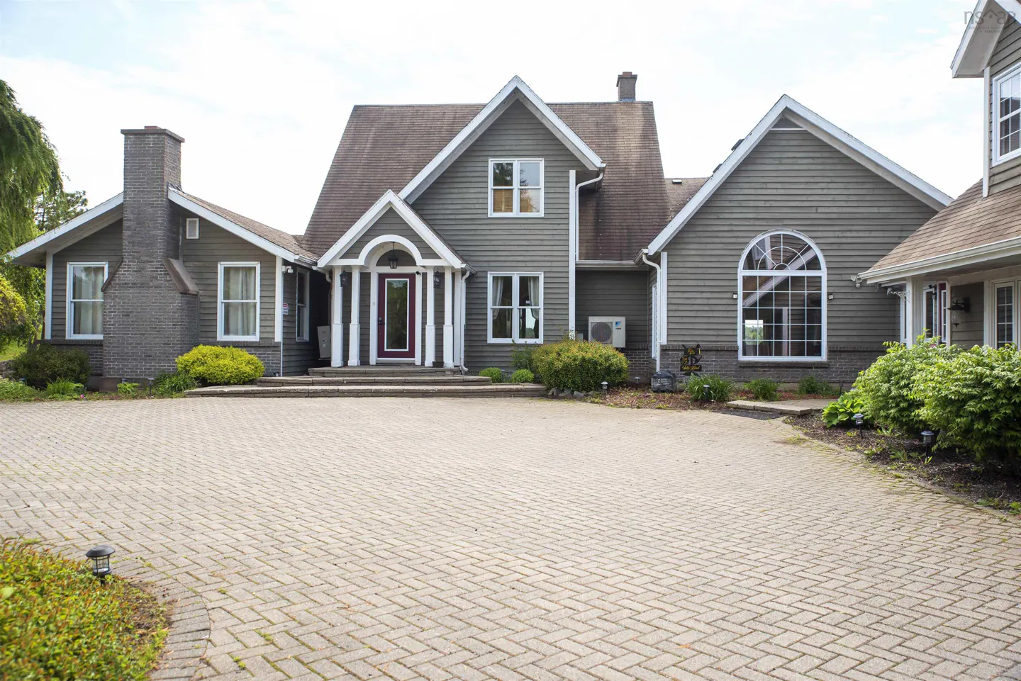 Exterior view of a large, gray house with a brick driveway and a red front door.