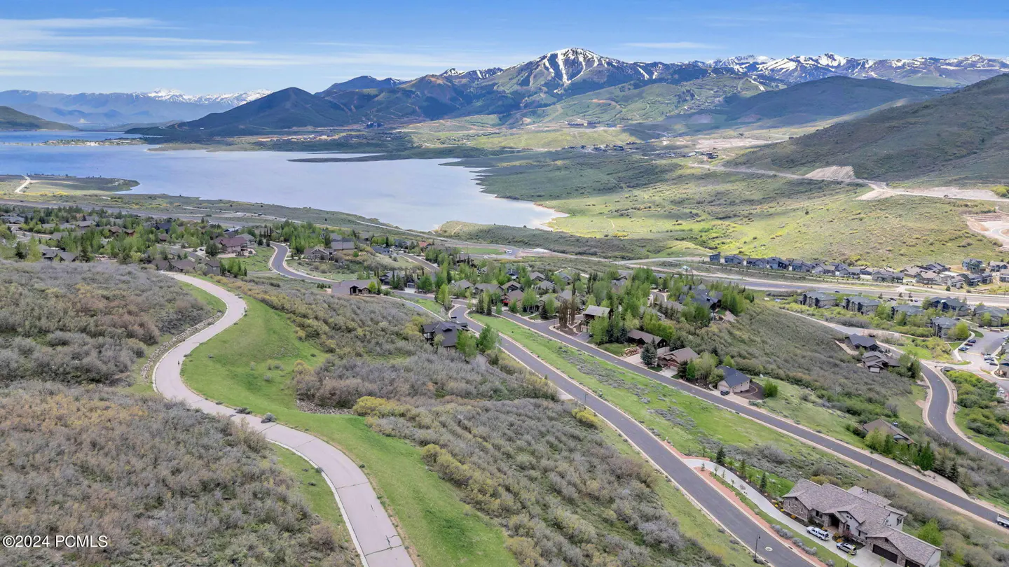 Aerial view of homes on a hillside overlooking a lake and snow-capped mountains under a blue sky.