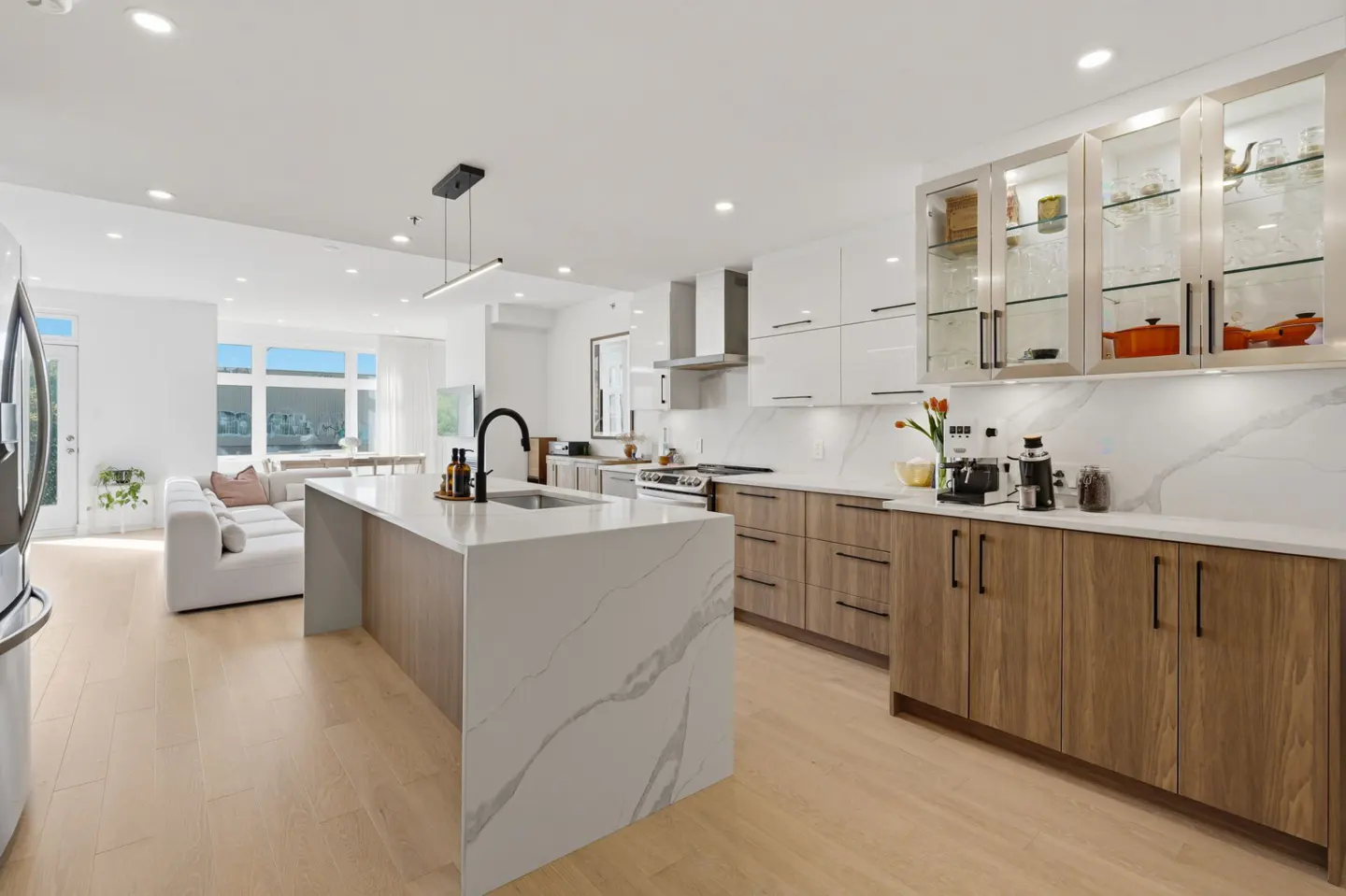 Modern kitchen with white marble island, wood cabinets, and open-concept living area with white sofa and light wood floors.