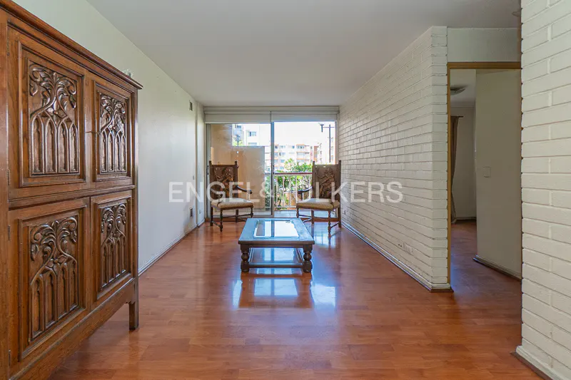 Living room with wood floors, a carved wood cabinet, two chairs, and a glass-topped coffee table. Balcony with city view.