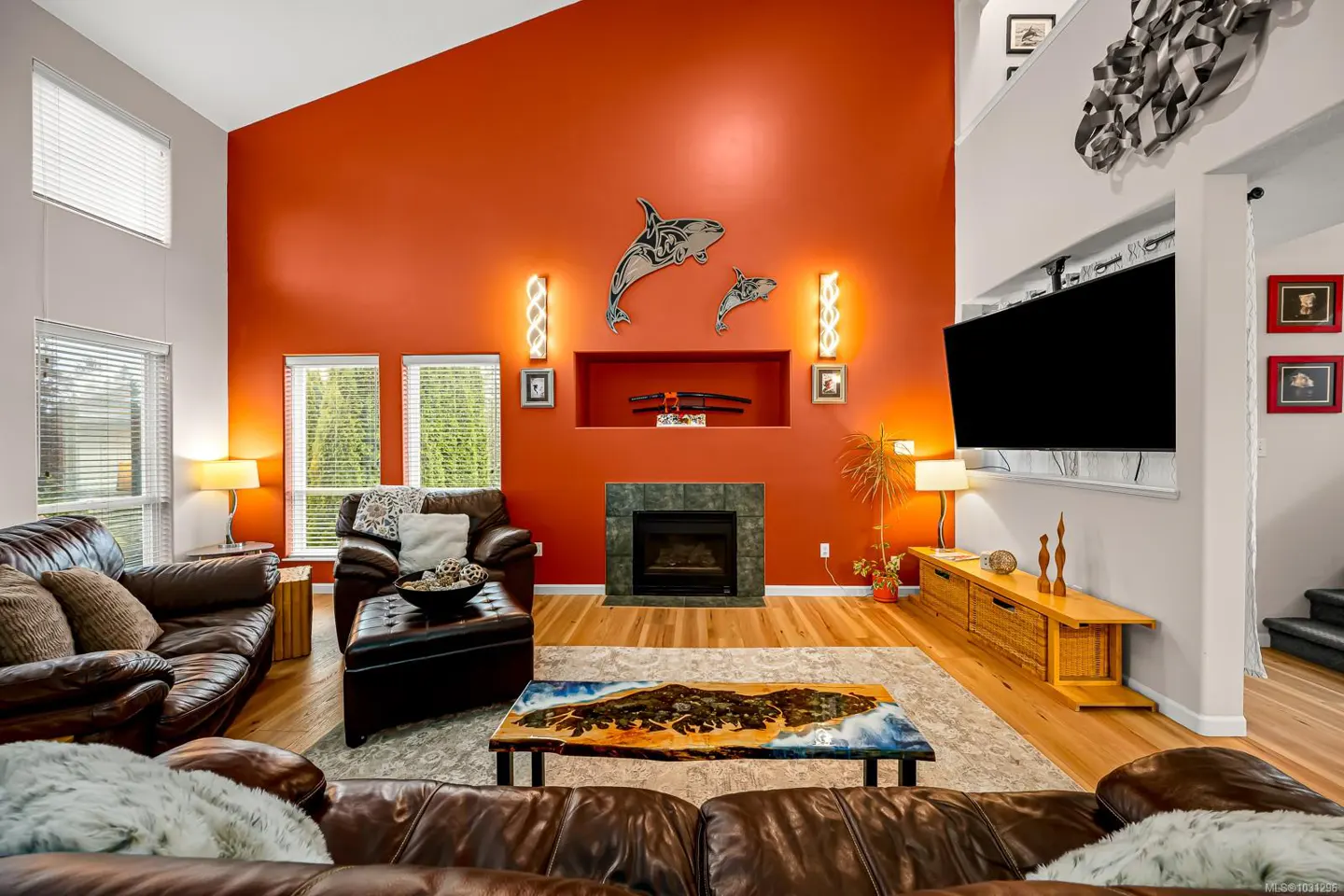 Living room with brown leather sofas, orange accent wall with orca art, fireplace, and a unique coffee table.