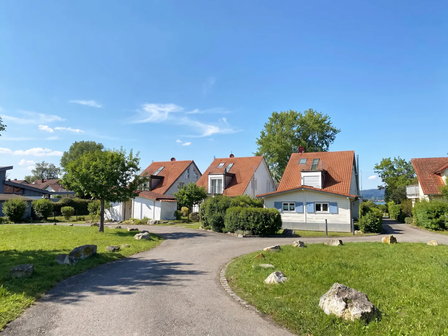 A sunny view of three white houses with red roofs, green lawns, and a gray paved road.