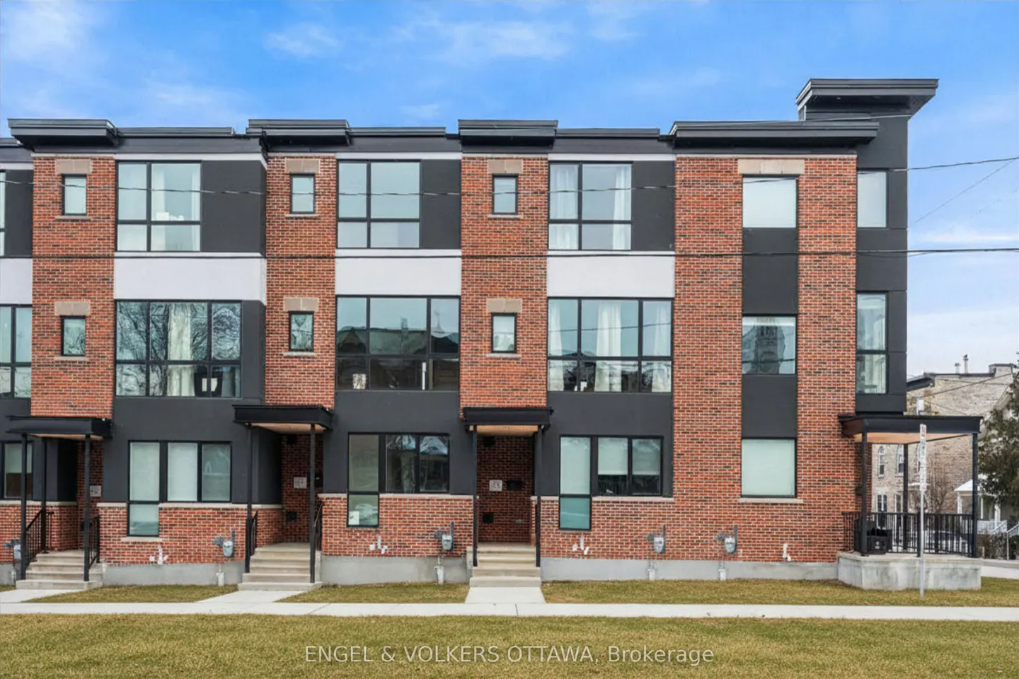 Three-story brick townhouses with black trim and large windows under a blue sky.