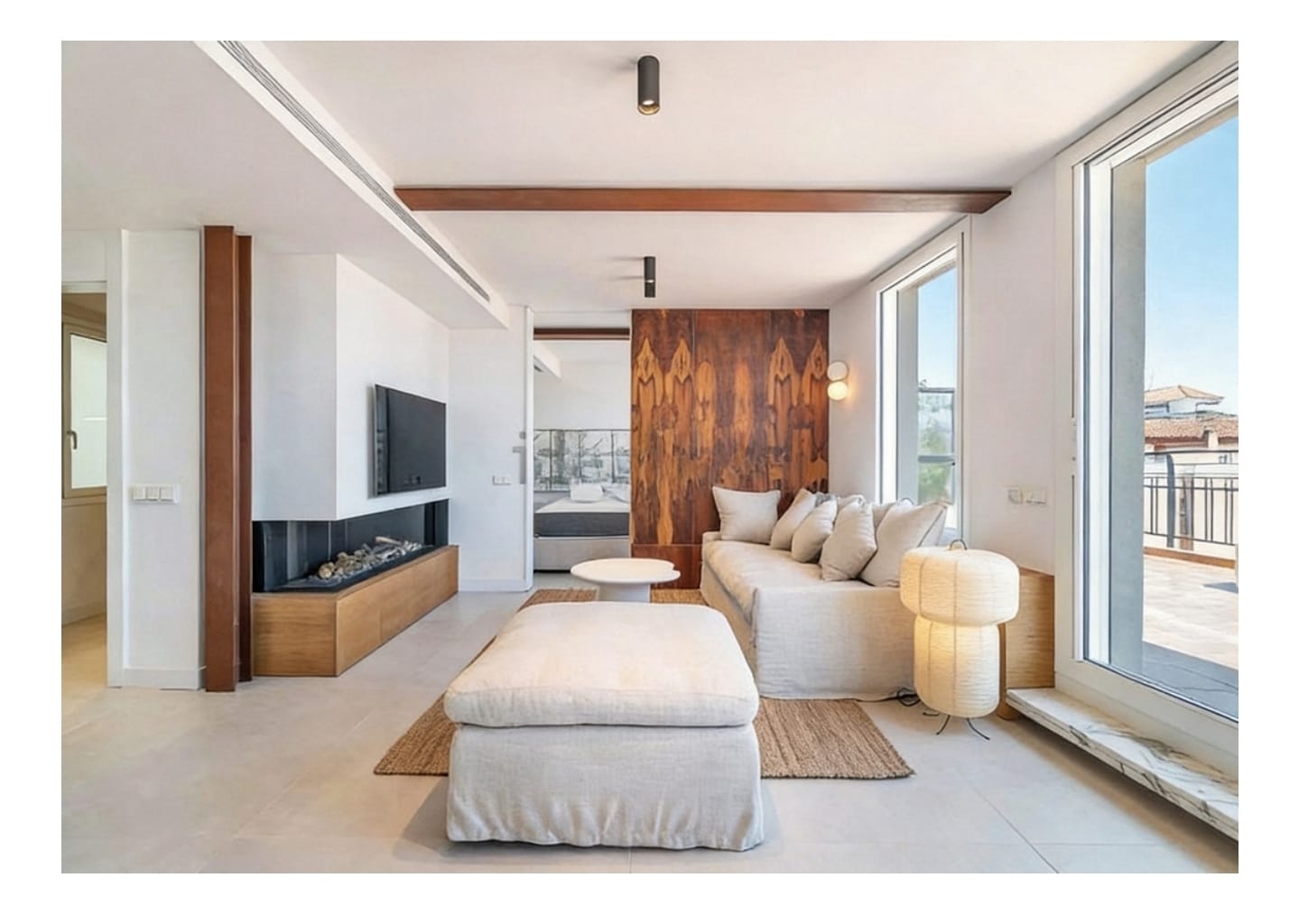 Modern living room with a beige sofa, large ottoman, wood-paneled wall, fireplace, and floor-to-ceiling windows. [AI-generated text]