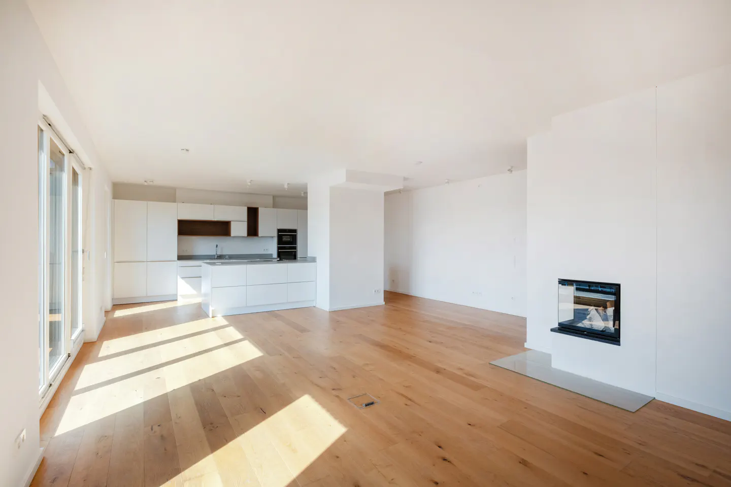 Bright, modern apartment with white walls, wood floors, and a sleek white kitchen. A fireplace is visible on the right.