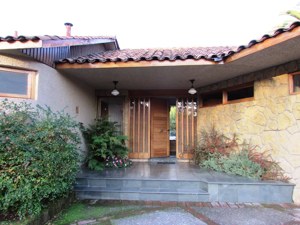 Front entrance of a single-story home with a stone facade, tile roof, and a wooden door flanked by slatted panels.