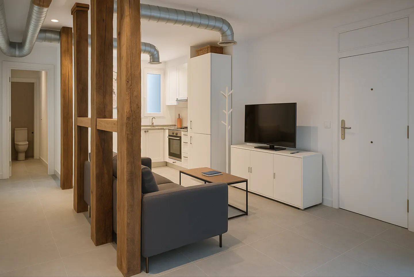 Living room with gray sofa, wood divider, and white kitchen. Exposed ductwork on ceiling. Toilet visible in hallway.