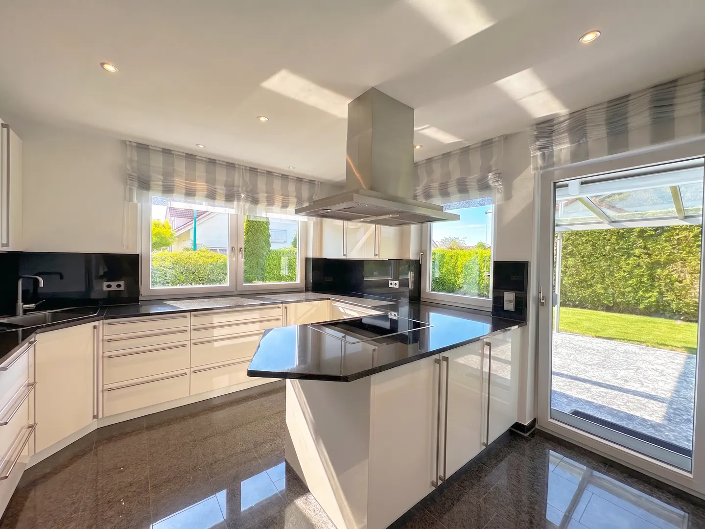 Bright kitchen with white cabinets, black countertops, and stainless steel range hood. Windows overlook a green yard.