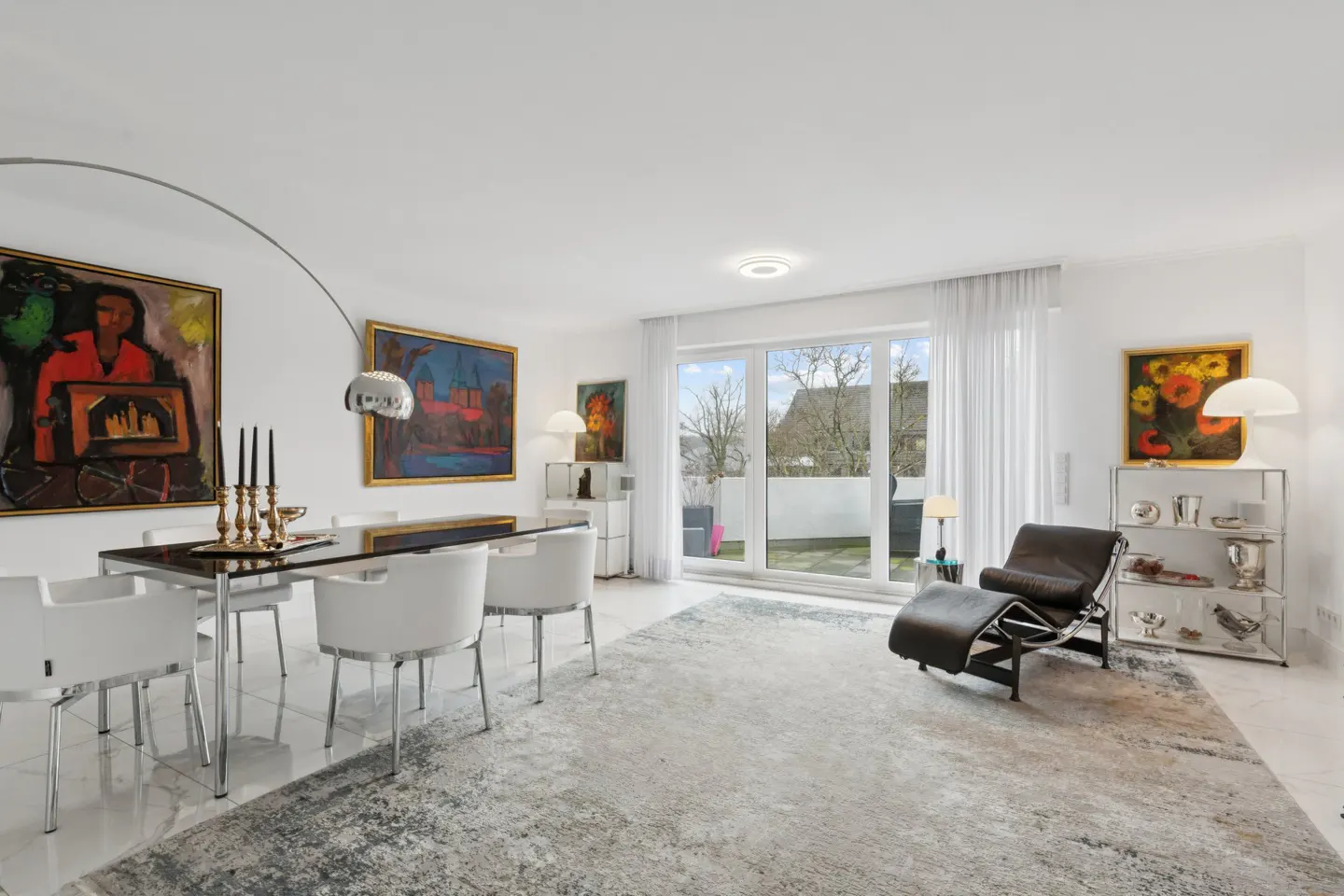 Bright, modern living room with white walls, a dining table with white chairs, and a black leather lounge chair near a glass door.