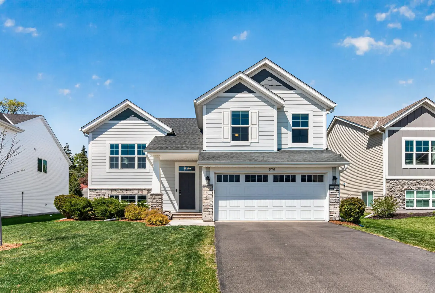 Two-story house with light gray siding, white trim, and a two-car garage on a sunny day.