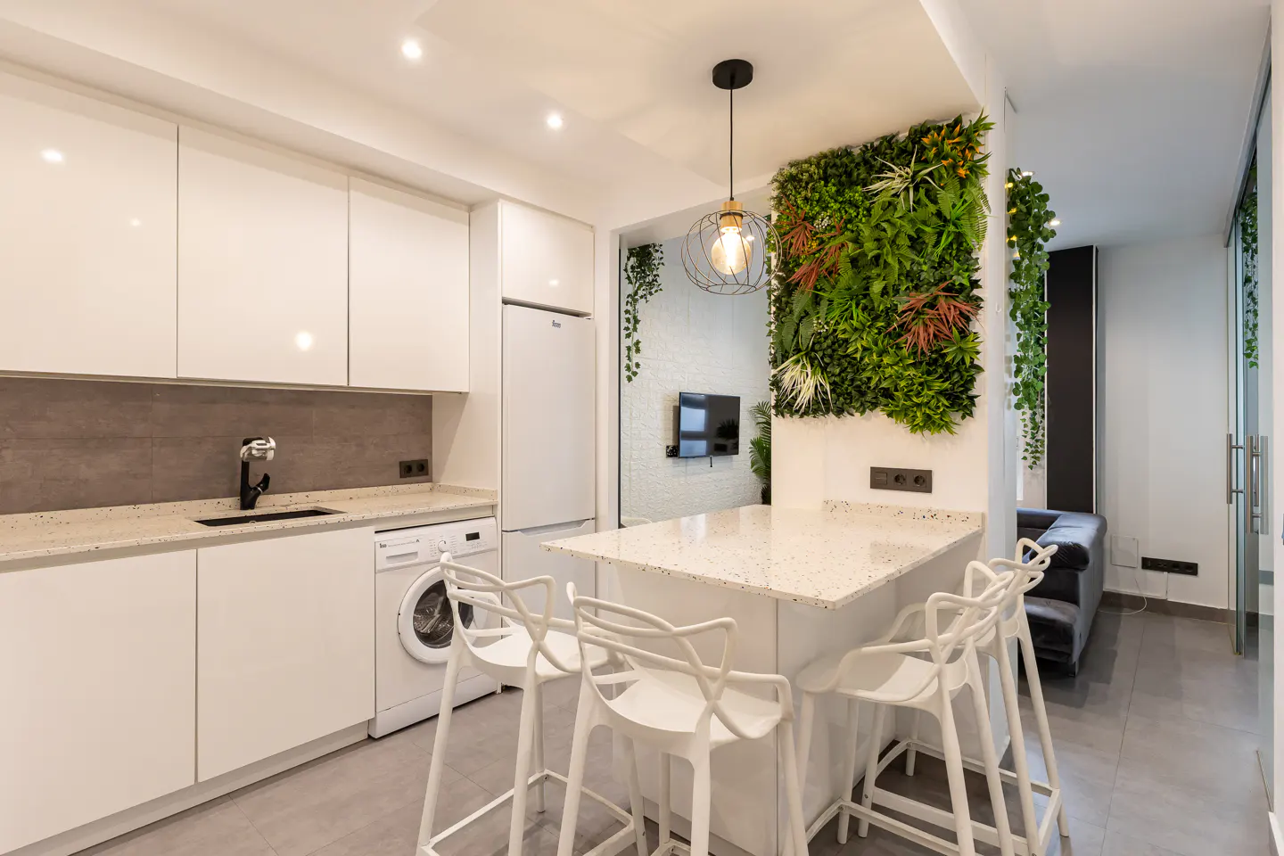 A modern kitchen with white cabinets, a breakfast bar with four white chairs, and a green wall.