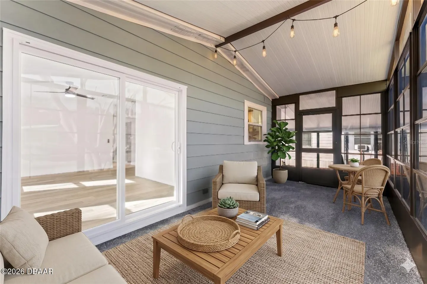 A sunroom with blue siding, a sliding glass door, and wicker furniture. String lights hang from the ceiling.