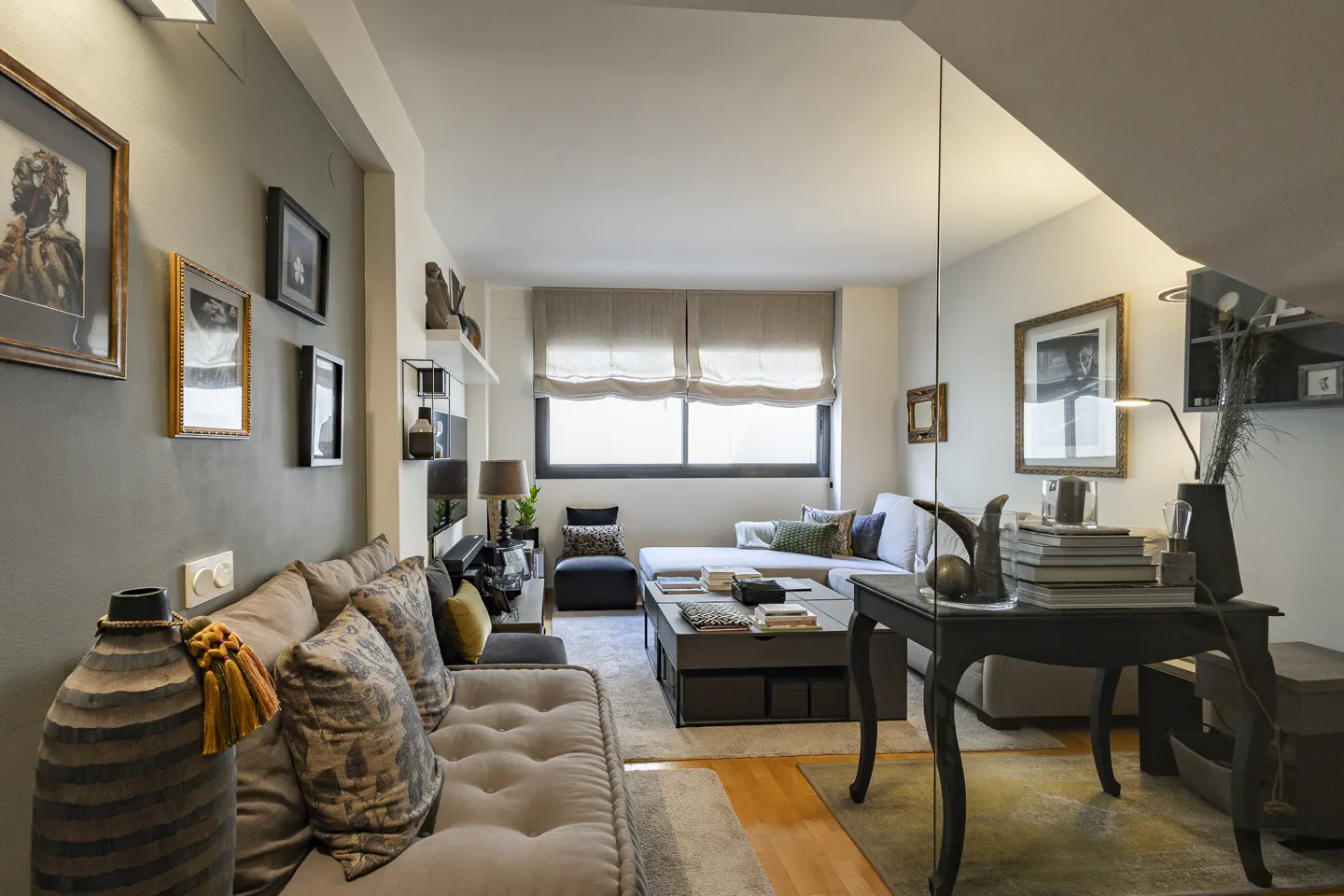 A modern living room with a gray sofa, patterned pillows, and framed art on a gray wall. A black table with books sits on a wood floor.
