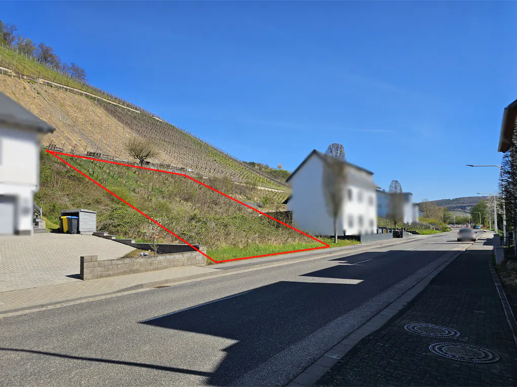 Vacant lot outlined in red, next to a road and hillside vineyard under a blue sky.
