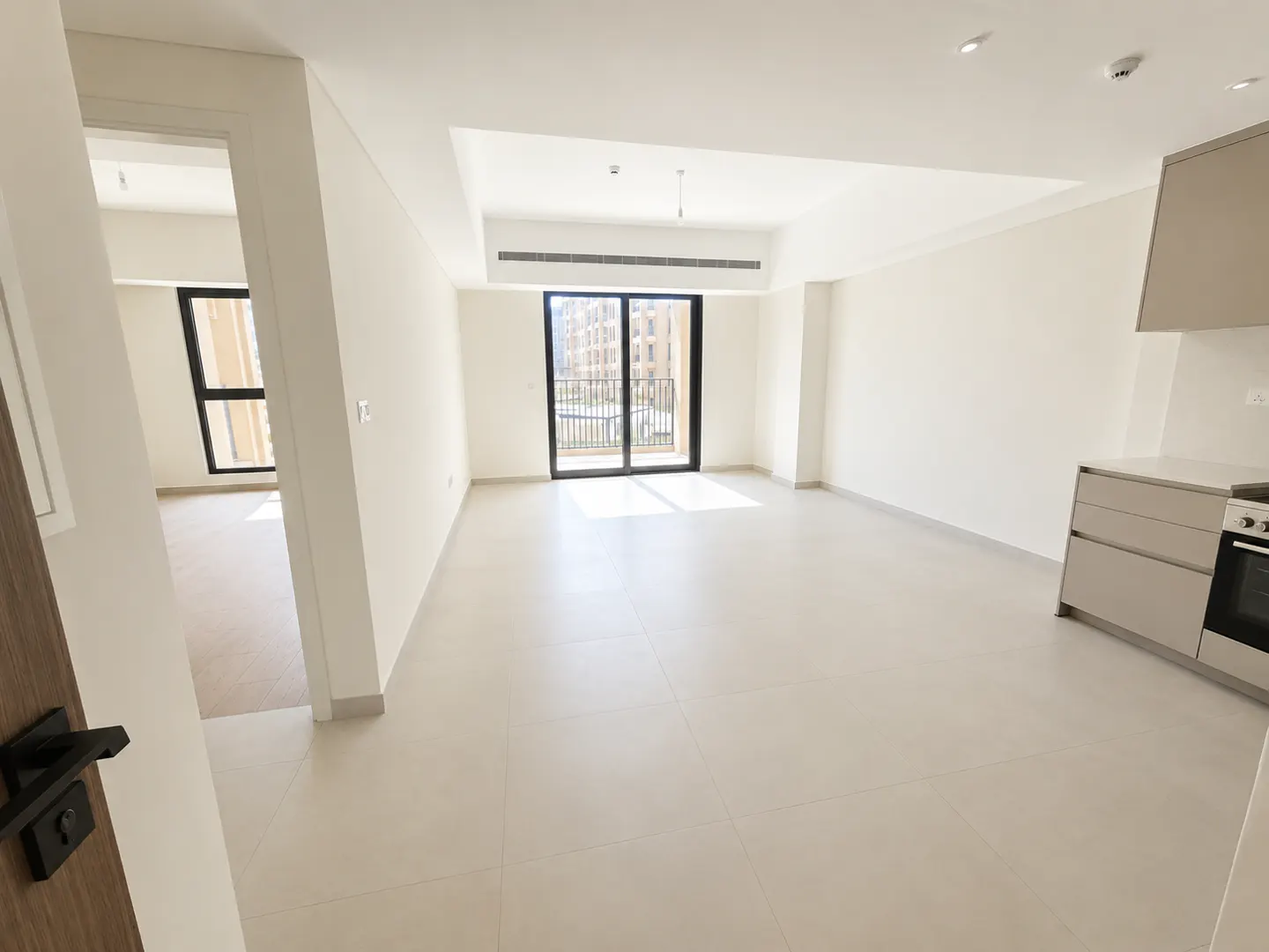 Unfurnished apartment with white walls, light tile floor, and a balcony with a view. Kitchen cabinets are visible on the right.