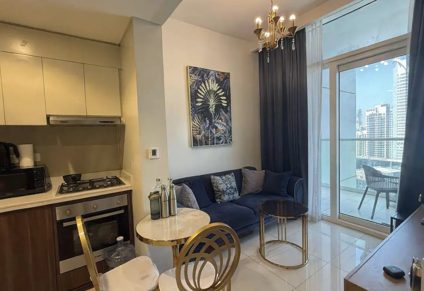 A modern apartment interior with a blue sofa, gold accents, and a balcony view of city buildings.