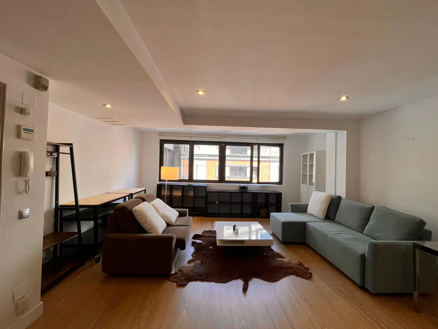 Spacious living room with wood floors, a brown sofa, a grey sectional, a white coffee table, and a cowhide rug.