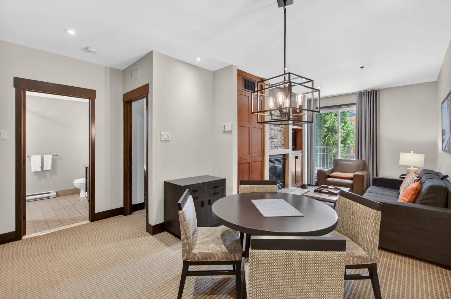 Interior view of a condo with a round dining table, chairs, and a living room with a sofa and fireplace.